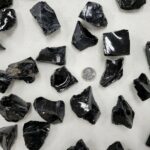 Collection of black obsidian crystals with shiny, glassy surfaces, arranged on a light background, showcasing their natural sharp edges and reflective qualities.