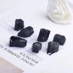 Collection of black tourmaline crystals on a white surface with a white decorative flower in the background, showcasing their natural texture and shape.