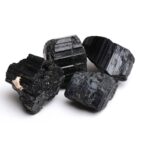 Four black tourmaline crystals with striated surfaces on a white background, showcasing their natural texture and geometric shape.