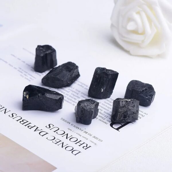 Collection of black tourmaline crystals on a white surface with a white decorative flower in the background, showcasing their natural texture and shape.