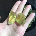 Two yellow citrine crystal specimens held on a person's hand, showcasing their translucent, vibrant yellow color and natural rough texture, ideal for science displays or decorative purposes.