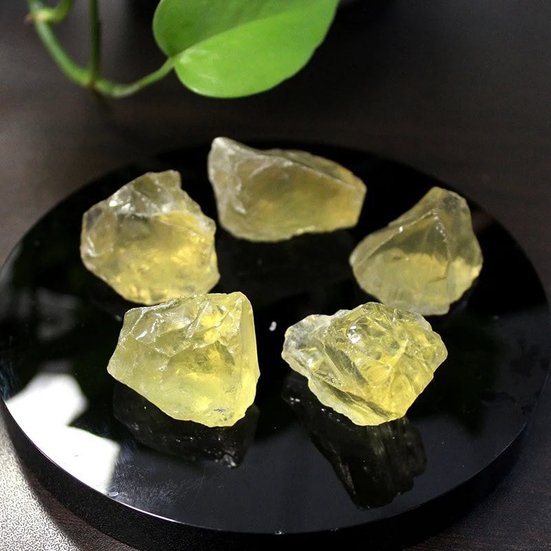 A close-up of six yellow citrine crystals displayed on a black circular plate, highlighting their translucent, rough texture and natural formation.