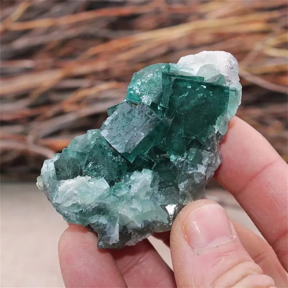 Close-up of a vibrant green emerald crystal held between fingers, showcasing its natural geometric structure and clarity.