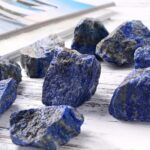 Close-up of vibrant blue lapis lazuli mineral rocks with gold pyrite inclusions, displayed on a white wooden surface for educational and decorative purposes.