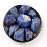 Lapis Lazuli mineral stones in a black bowl, showcasing their deep blue color with gold and white mineral inclusions, used for educational purposes and decorative displays.