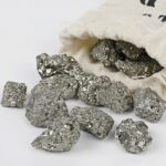 Close-up of metallic silver pyrite mineral rocks spilling from a cloth bag, showcasing their shiny, crystalline surface.