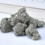 Close-up of metallic gray galena mineral rocks with a shiny, reflective surface, placed on a white background near a book.