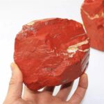 Hand holding a large red sedimentary rock with layered textures, showcasing natural geological formations.