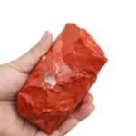 Hand holding a red iron ore rock, showcasing its rough texture and vibrant color, ideal for educational science demonstrations and decor.