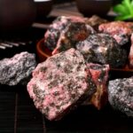 Pink and black mineral rocks with rough texture, displayed on a black surface.