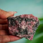 Hand holding a pink and black mineral rock with a textured surface, close-up shot.