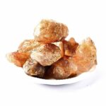 Group of large, raw salt rocks displayed on a white plate, showcasing their natural crystalline structure and earthy orange-brown hues, ideal for science experiments and educational demonstrations.