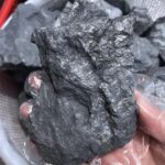 Close-up of a black obsidian volcanic glass rock showing its smooth, shiny surface and natural fractures.