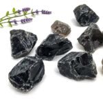 Collection of black obsidian crystals with a sprig of lavender on a white background, showcasing their natural glossy appearance and sharp edges.