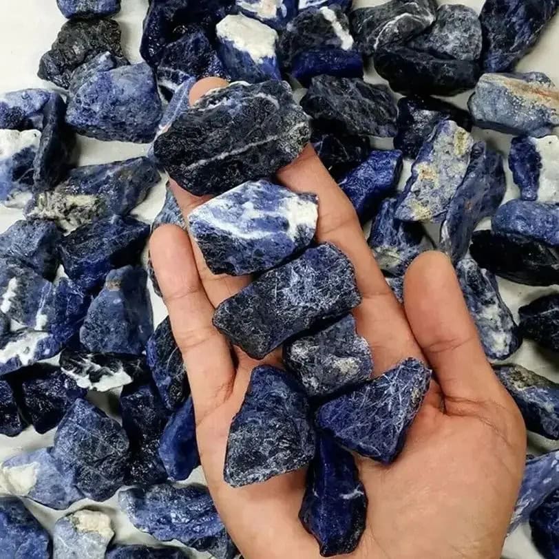 Hand holding a collection of blue obsidian crystal rocks, showcasing their deep blue color and natural textures, ideal for healing, meditation, and decorative purposes.