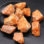 Irregularly shaped Himalayan salt rocks with a warm orange hue displayed on a black plate. Perfect for educational displays, decor, or salt therapy.