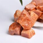 Natural Himalayan salt crystals with a pink-orange hue, displayed on a white surface, showcasing their rough texture and mineral-rich composition.