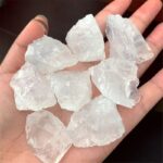 Hand holding multiple raw clear quartz crystals, showcasing their natural, unpolished form with a transparent appearance.