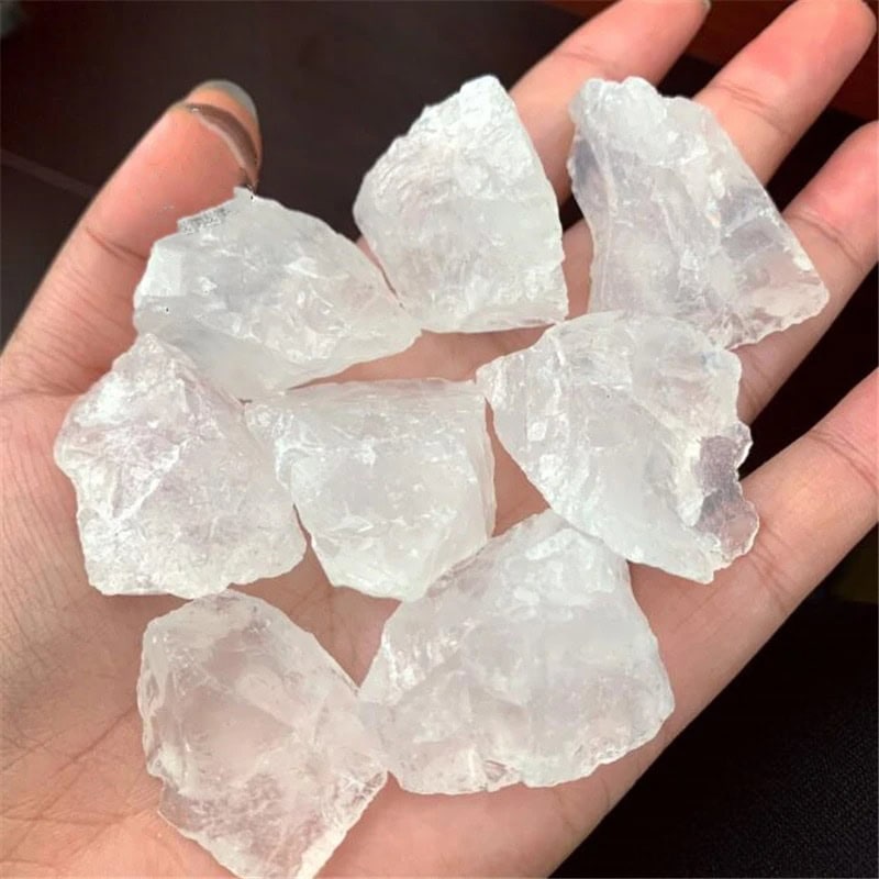 Crystal Quartz Raw Stones Hand holding multiple raw clear quartz crystals, showcasing their natural, unpolished form with a transparent appearance.