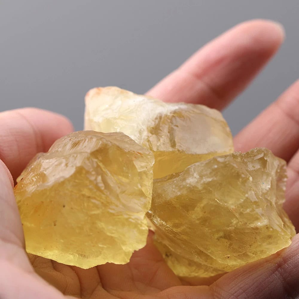 A close-up of several raw yellow citrine crystals held between fingers, showcasing their translucent, golden-yellow color and natural, rough texture.