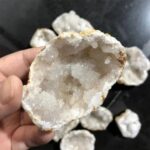 Close-up of a white geode mineral with sparkling crystalline interior, held in hand with other geodes in the background.