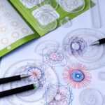 Transparent geometric drawing templates with colorful patterns and pens on a white surface.