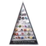 Collection of various colorful gemstones including aquamarine, amethyst, ruby, sapphire, and more, arranged in a pyramid-shaped display case.