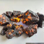 Close-up of volcanic rocks with glowing orange lava-like cracks, showcasing natural mineral formations and volcanic activity.