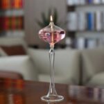 Pink liquid-filled glass candle holder with a lit candle inside, placed on a wooden surface in a cozy living room.