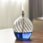 Elegant glass oil lamp with a swirling design, blue base, and a small flame on top, perfect for science decor and educational demonstrations.