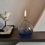 Elegant glass oil diffuser with blue liquid and a small flame on top, serving as a decorative science gadget for home or office.