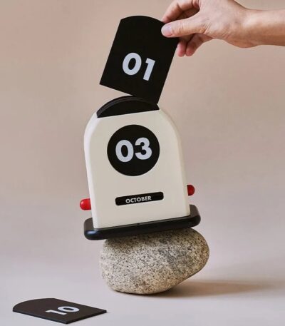A playful October flip calendar with black and white cards displaying the date, balanced on a smooth stone, perfect for educational and decorative purposes.