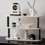 Modern desk decor featuring a white flip calendar clock displaying the date "23 March" alongside minimalist decorative items including a textured white sculpture, black and white containers, and a sma.