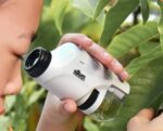 A child examining leaves with a handheld microscope in a garden.