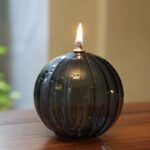 Elegant black glass candle with a lit flame, showcasing a sleek spherical design perfect for home decor and educational science displays.