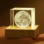 Realistic 3D moon lamp featuring detailed lunar surface, encased in a clear acrylic cube and mounted on a wooden base, perfect for educational decor and space enthusiasts.