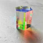Colorful holographic hexagonal prism optical crystal with rainbow reflections on a textured surface.