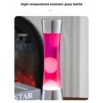 Modern lava lamp with pink wax inside a high-temperature resistant glass container, featuring metallic silver top and bottom, placed on a wooden surface near a black appliance.