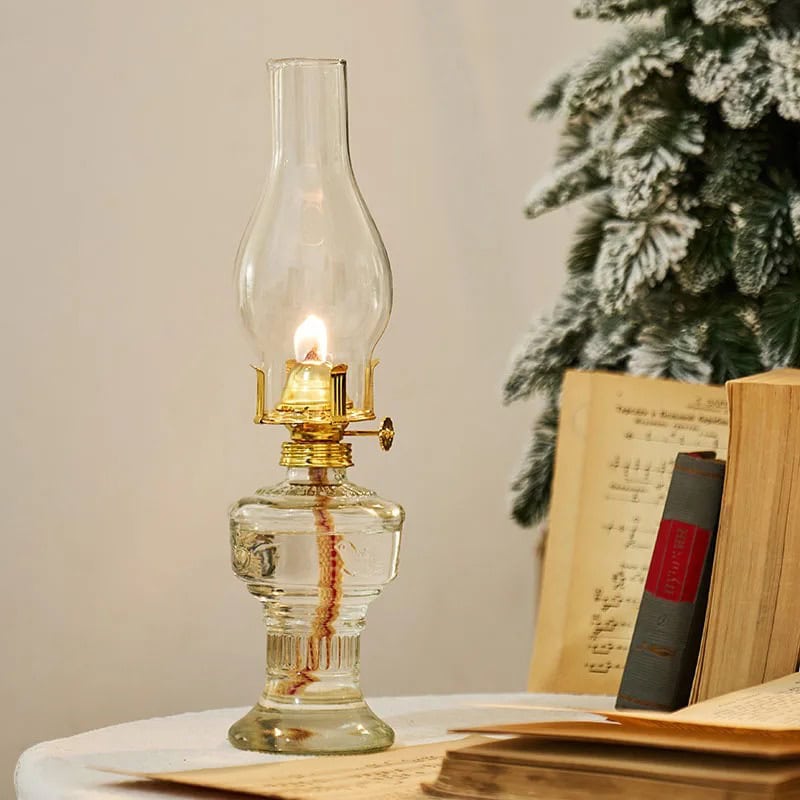 Vintage oil lamp with a lit flame on a white surface, surrounded by books and a snow-dusted Christmas tree in the background. Perfect for science decor and educational settings. 70s Style Oil Lamp - Image 1