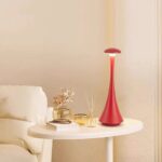 Red modern table lamp with a sleek, futuristic design on a white side table.