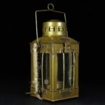Antique brass lantern with glass panels, vintage design, suitable for decor or collection. Features a handle and intricate metal details, evoking a nostalgic, historical ambiance.