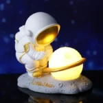 Adorable astronaut figurine holding a glowing planet lamp with a golden ring, set against a starry night background. Perfect for space-themed decor and educational toys.