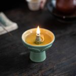 Small ceramic oil lamp with a lit wick, placed on a dark wooden surface, demonstrating traditional lighting methods.