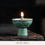 Ancient oil lamp with a lit flame, made of green ceramic, placed on a rustic wooden surface.