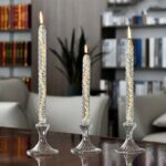Three lit candles in elegant glass holders on a wooden table, creating a warm and cozy atmosphere in a modern living room.