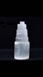 Transparent tiered ice sculpture with multiple stacked blocks, illuminated against a dark background, showcasing its crystalline structure and artistic design.