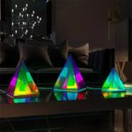 Colorful illuminated geometric pyramid decorations on a black table in a modern living room setting.