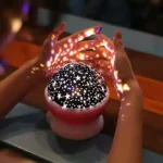 Hand holding starry sky LED night light projecting star patterns onto hands, creating a magical celestial display.