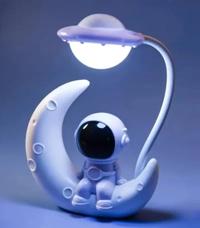 Adorable astronaut toy resting on a moon-shaped stand illuminated by a planet-shaped lamp, perfect for space-themed decor or educational purposes.