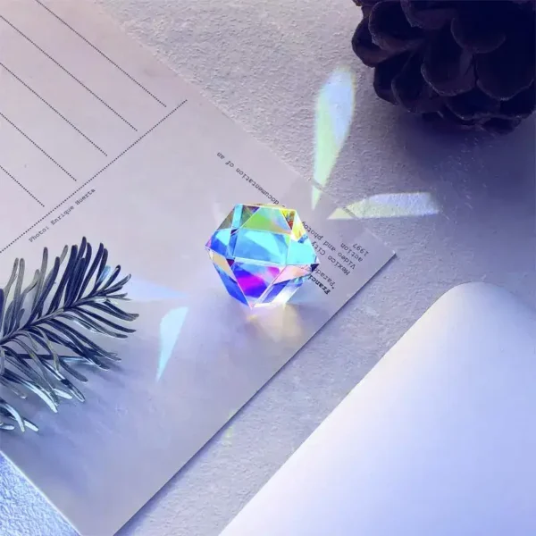 A colorful crystal prism on a white surface creating rainbow light reflections, with a pine branch and a pine cone nearby.
